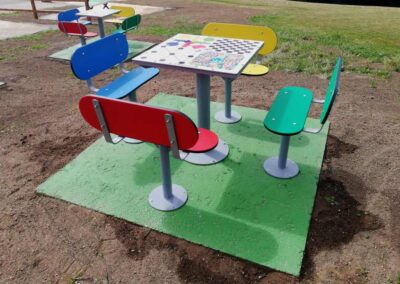 Tables multi-jeux avec bancs de couleur aménagés dans un parc.
