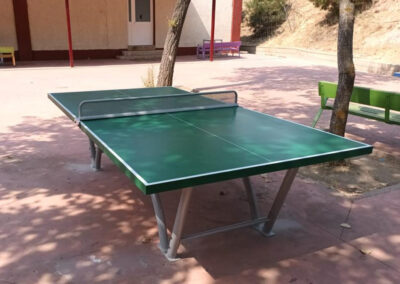 Une table de ping-pong Sport verte installée dans une cour de récréation.